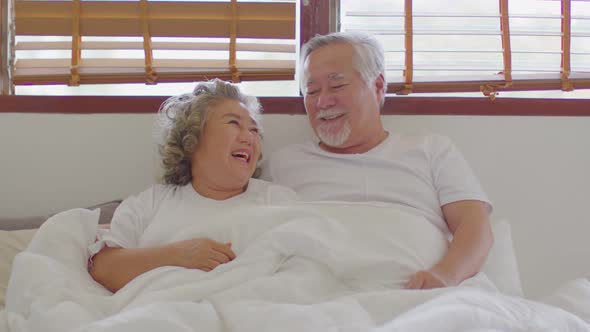Happiness Two Asian couple elder husband and wife lying on bed together smile and laughing at home