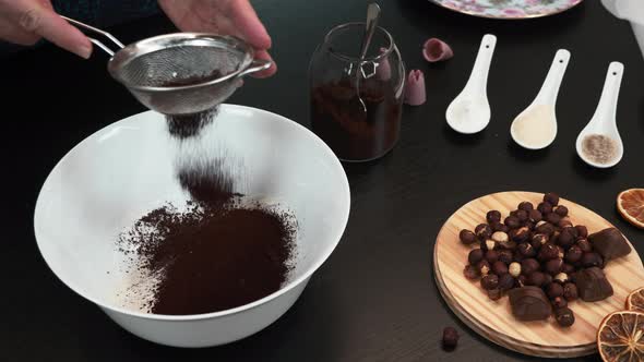 Female is sifting cocoa powder and adding it to flour. Woman is baking pastry at home.