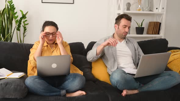 Tired From Work on the Distance Middleage Couple Sitting Separate on the Couch with Laptops