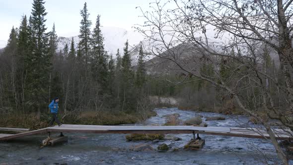 A Man Traveler Crosses a Mountain Stream Over a Bridge. Beautiful View.