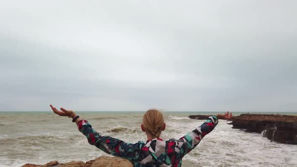 Girl Raises Her Hands Up While Standing with Her Back on the Seashore During a Storm.
