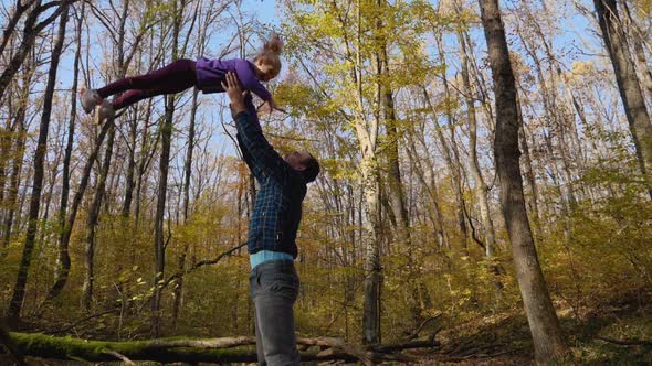 In slow motion, a father tosses his daughter while standing in an autumn forest
