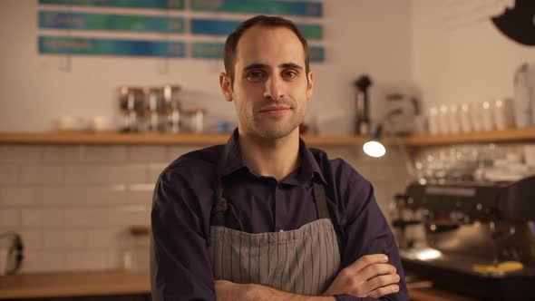 Male Caucasian Barista Wearing Apron Standing with Folded Hands and Lightly Smiling in Slowmotion