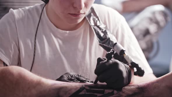 A Session at the Tattoo Salon  Young Man Tattooing Big Letters on the Leg  Looking in the Camera