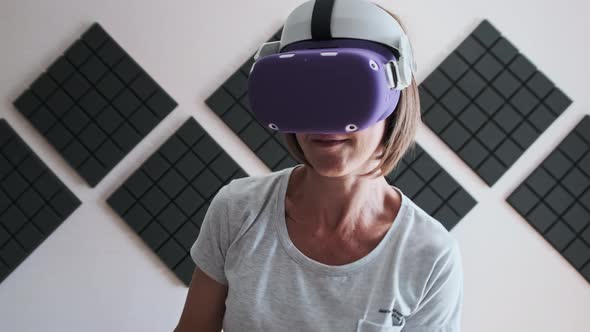 Young Woman in a Virtual Reality Headset Plays a Game at Home