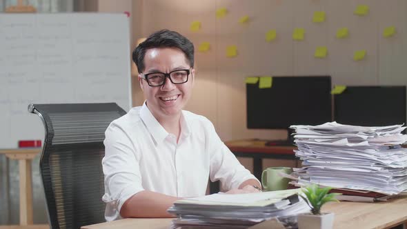 Asian Man Smiling To Camera While Working With Documents At The Office