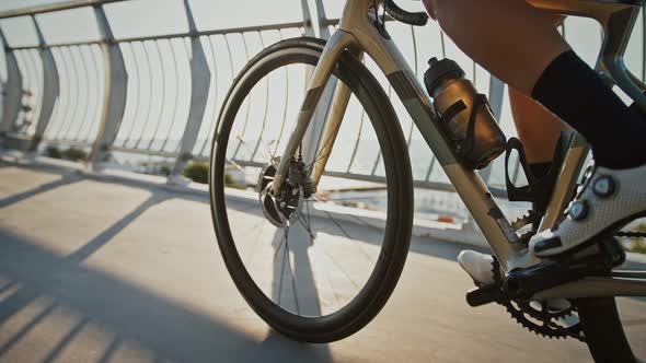 Legs of Professional Cyclist in Cycling Shoes Who Riding a Bike Uphill Along Bridge Near a Sea