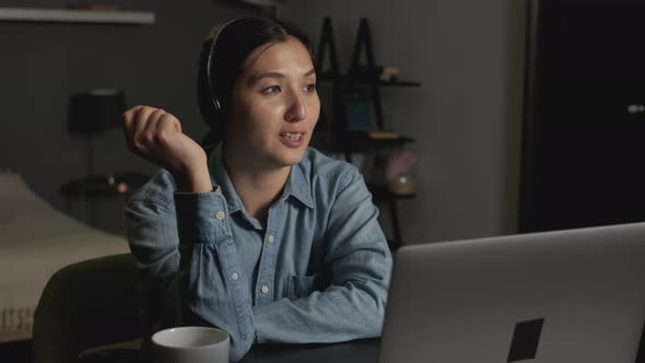 Close-Up of a Young Asian Woman in Headphones with a Microphone Chatting with Friends or a Client