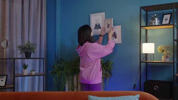 Happy Young Woman Putting Modern Picture in Frame on Blue Wall Decorating Living Room at New Home