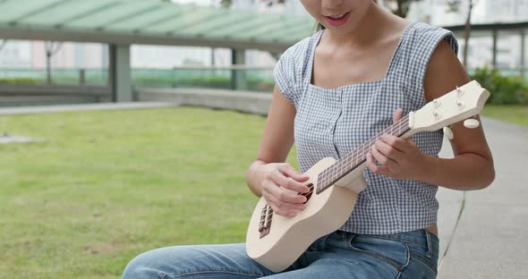 Woman play a song on ukulele at outdoor park