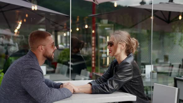 Man and Woman are Resting in Cafe Sitting at Table in Open Terrace Holding Hands