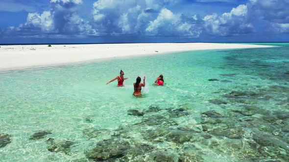 Female models sunbathing on tropical shore beach vacation by aqua blue water and clean sandy backgro