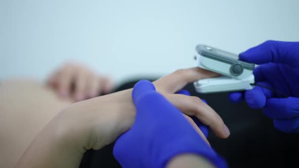 Closeup Doctor Putting on Pulse Oximeter on Finger of Patient Lying on Examination Couch