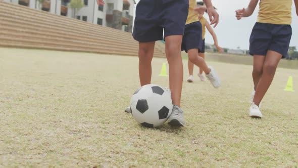 Video of legs of diverse girls playing soccer in front of school