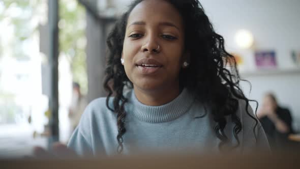 Happy African woman wearing blue sweater talking by video call on laptop
