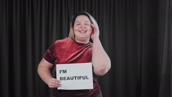 A Confident Flirty Fat Woman Holding a Nameplate with a Sign I'M BEAUTIFUL