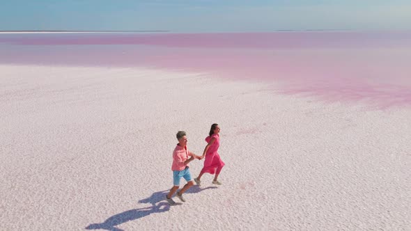 Aerial Drone Footage of Happy Young Couple in Pink Wear Having Fun and Joyfully Running on White