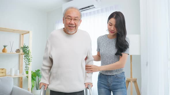 Asian young daughter take care and support senior older man walk with walker at home.