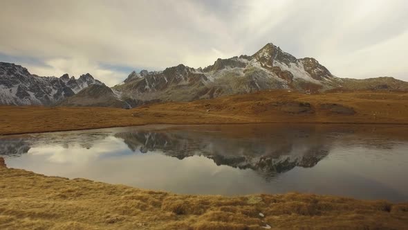 Side POV Walking on Fall Valley Lake and Snowy Mounts Approaching Sunset