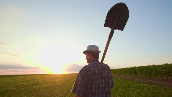 Rear View of a Farmer with a Shovel Walking Through the Field