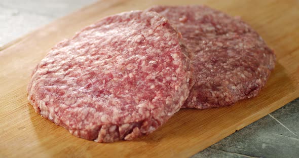 Raw Burger Meat Slowly Rotates on a Wooden Board.