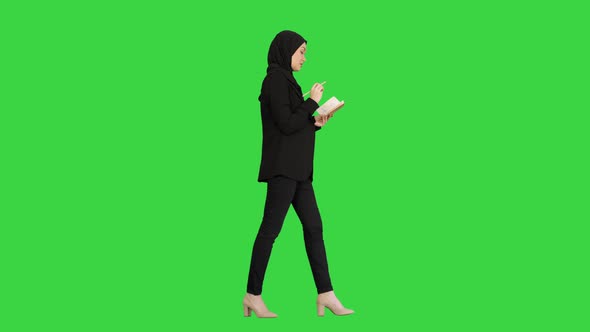Muslim Businesswoman Thinking and Writing Ideas in Her Notepad While Walking on a Green Screen
