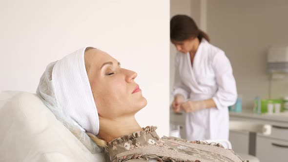 Woman on the Beautician's Couch Doctor Preparing Injection in the Background