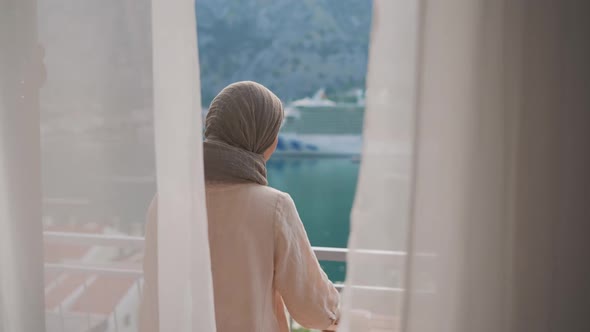 Arab Young Muslim Woman in Hijab Opening Curtain Lace Enjoying Drinking Hot Coffee or Tea Watching