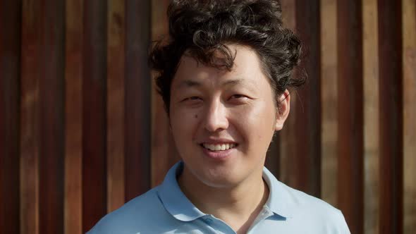 Portrait of Middle Aged Asian Man in Blue Shirt Standing Against Decorative Wooden Wall Background