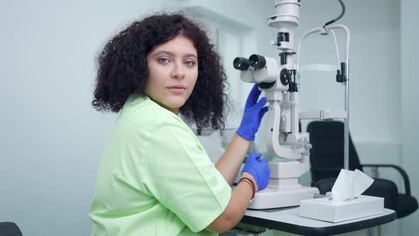 Professional Doctor Adjusting Equipment in Ophthalmologic Clinic Turning Looking at Camera Smiling