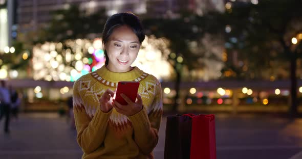 Woman use of mobile phone use of mobile phone with shopping bag in city at night