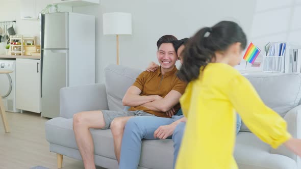 Asian attractive LGBTQ gay family sit on sofa, playing with young girl kid in living room at home.