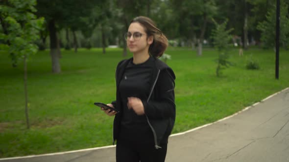 A Young Woman is Jogging with a Phone in Her Hand and Rejoices