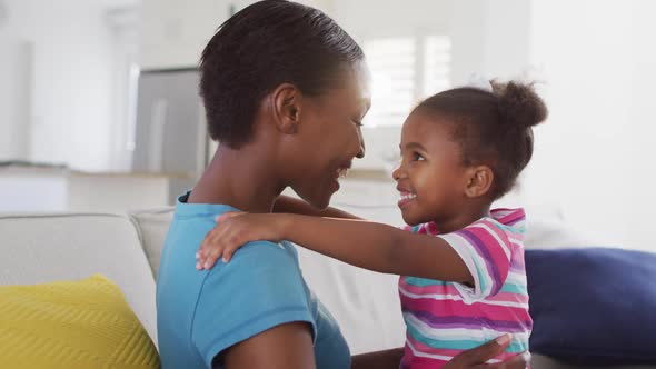 Happy african american mother and daughter sitting on sofa and touching foreheads