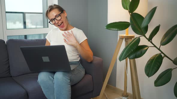 Casual Dressed Woman with Glasses Sitting on the Sofa and Communicates Via Video Link with Family or