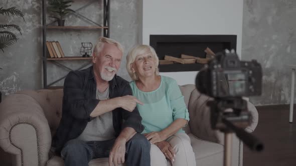 Technology, Blogging and People Concept - Happy Smiling Senior Couple with Camera Recording Video