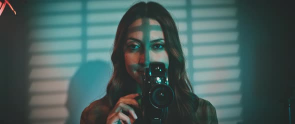 A beautiful woman looking at the camera and holding an old vintage camera