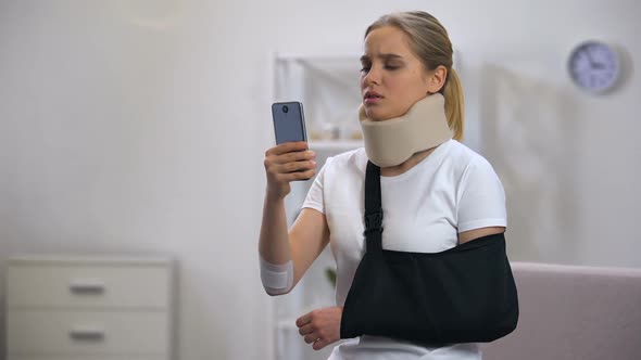 Sad Female in Foam Cervical Collar and Arm Sling Reading Message on Smartphone