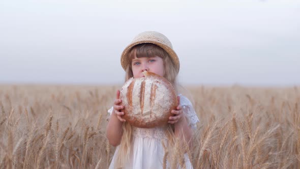 Bread Grower Kid Girl, Small Fair Haired Farmer Daughter Bites Tasty Baked Bread and Smiles Standing