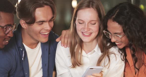 Close Up of Young Smiling Woman Showing Smartphone Content To Her Friends. Group of Cheerful