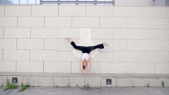 Woman doing a handstand and moving legs in front of wall