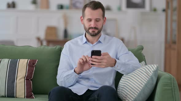 Serious Young Man Using Smartphone on Sofa