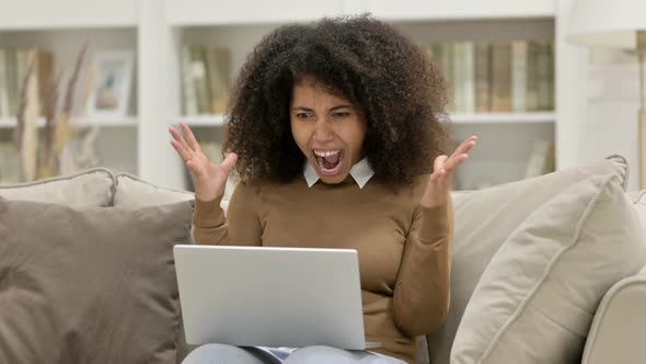 Excited Young African Woman with Laptop Celebrating on Sofa