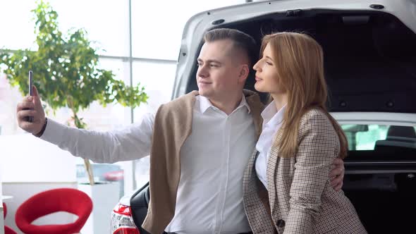 Happy Couple Taking a Selfie at a Car Dealership with a New Car in the Background