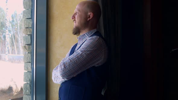 Young Dominant Man Leaning Against the Wall Looks Thoughtfully at the Winter Landscape From the