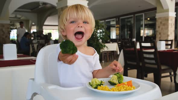 Little Boy Holds Broccoli in His Hand and Stretches Forward