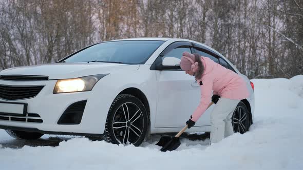 Female Digging Snow with Shovel From Wheel of Car