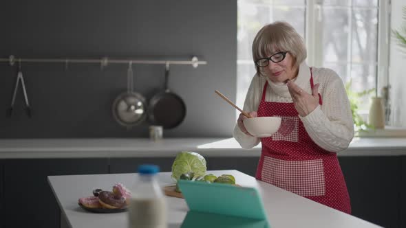 Portrait of Positive Caucasian Female Retiree Smelling Food in Bowl Mixing Sauce Ingredients