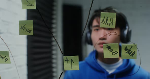 Young Man Listens to Music in Headphones and Planning on the Glass Wall