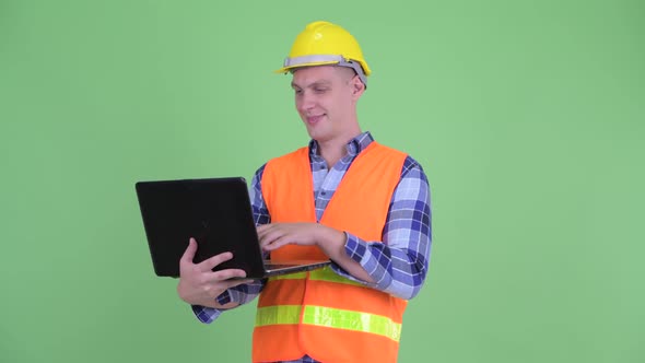 Happy Young Man Construction Worker Thinking While Using Laptop